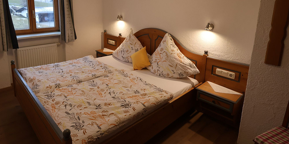 Erstes Schlafzimmer der Ferienwohnung Grüntenblick mit Doppelbett, Leselampen und Fensterblick – ideal für Eltern im Allgäu-Urlaub