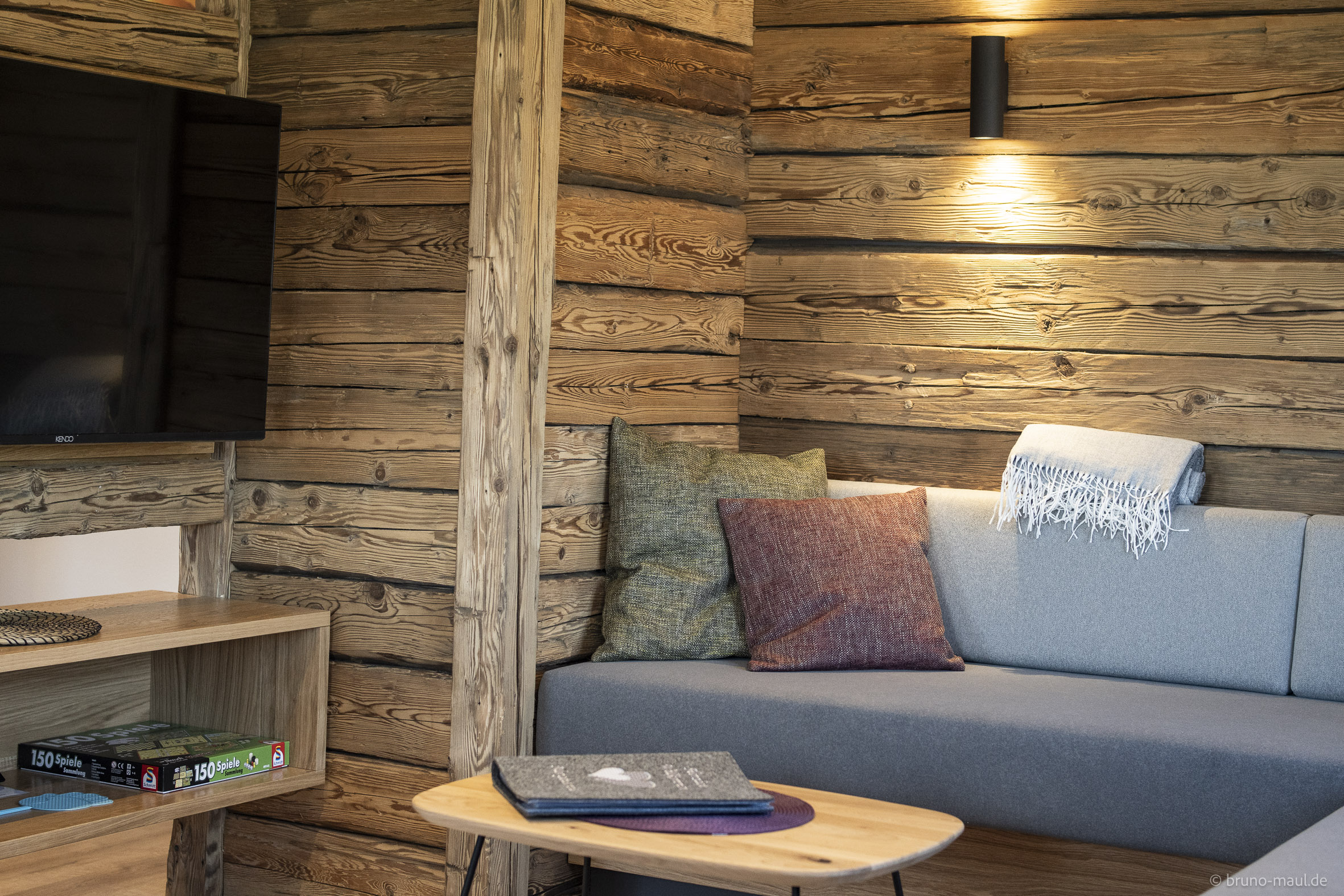 Gemütliche Sitzecke mit Naturholzverkleidung, Sofa, Kissen, Spielesammlung und TV – Ferienwohnung Morgensonne im Allgäu