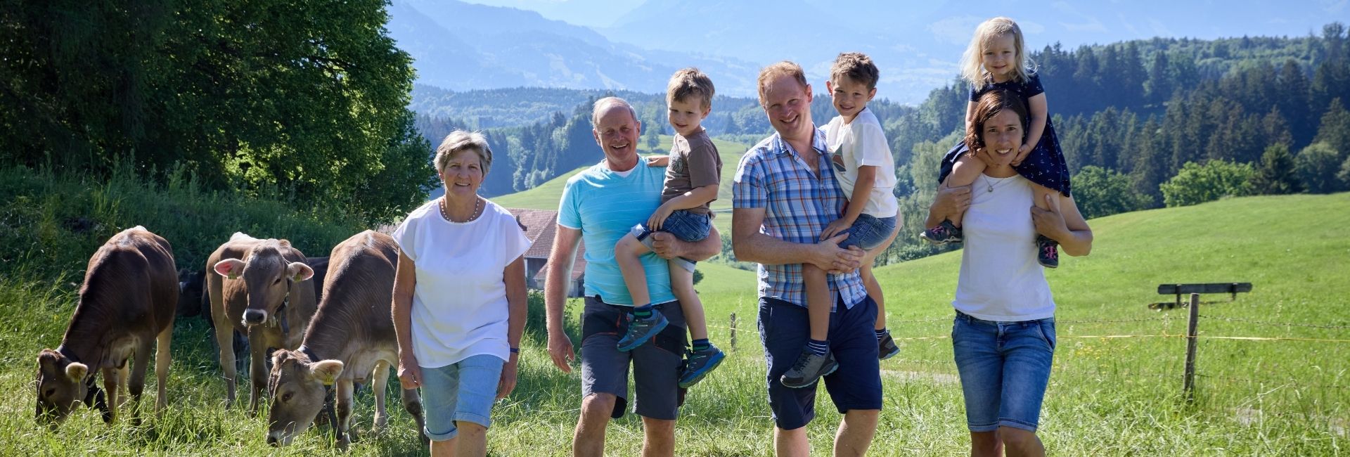 Gastgeberfamilie des Ferienhof Eger mit Kindern und Kühen vor der Bergkulisse in Bayern